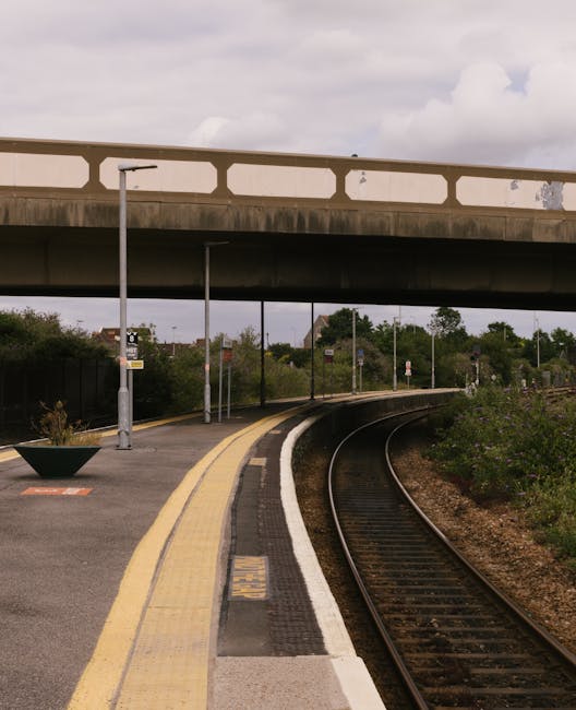 A deserted railway platform with a curved track running alongside, featuring a yellow safety line along the edge and textured tactile paving for visually impaired pedestrians. The platform has a moder